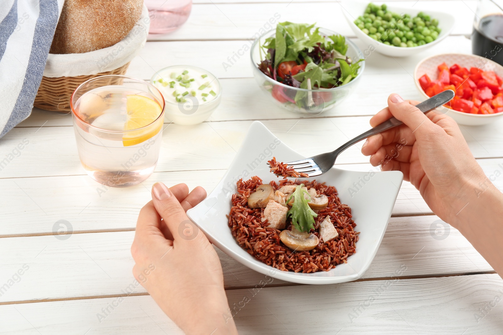 Photo of Woman eating tasty brown rice with meat and vegetables at white wooden table, closeup