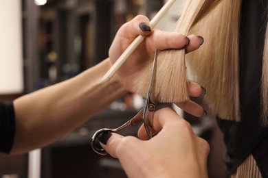 Photo of Professional hairdresser cutting woman's hair in salon, closeup