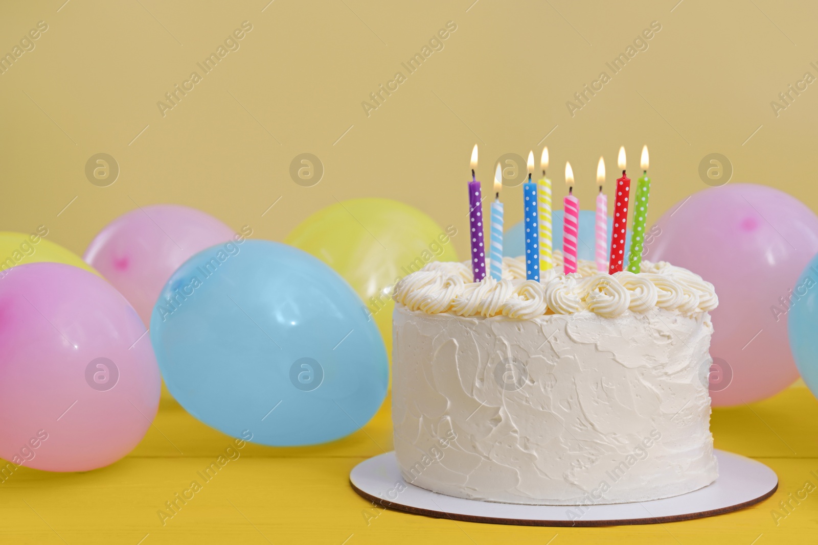 Photo of Delicious cake with burning candles and festive decor on yellow background. Space for text
