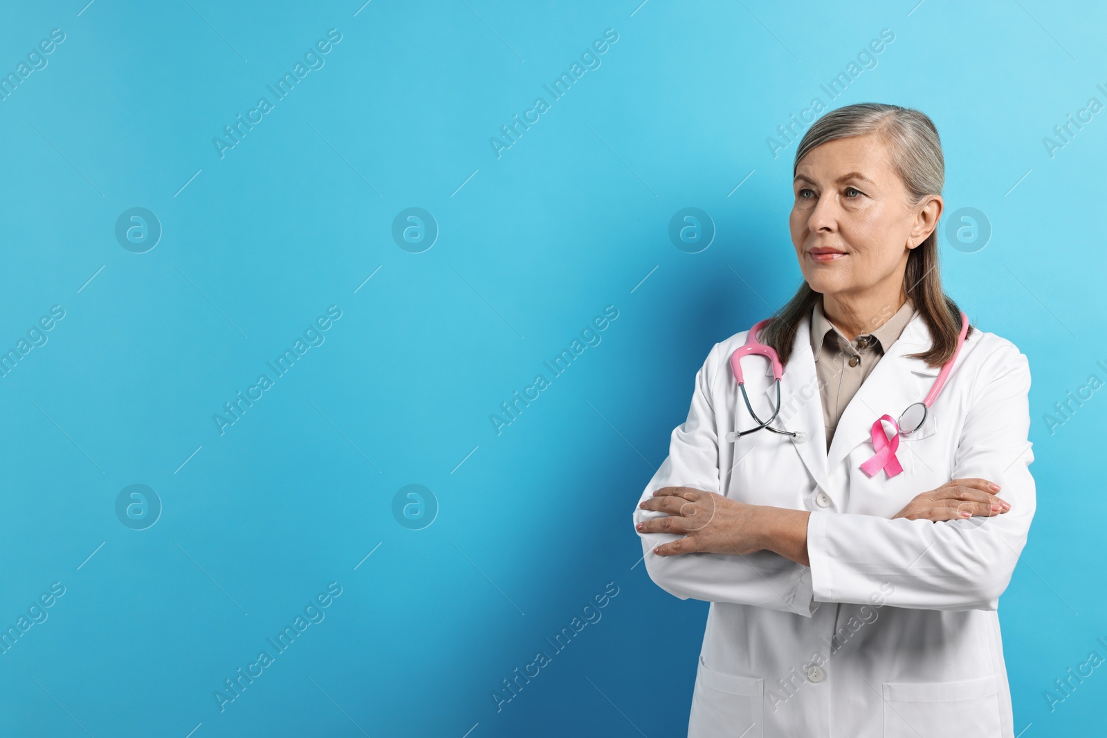 Photo of Mammologist with pink ribbon on light blue background, space for text. Breast cancer awareness