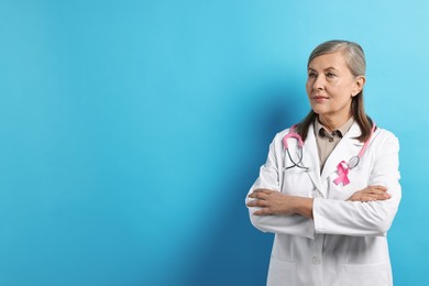 Photo of Mammologist with pink ribbon on light blue background, space for text. Breast cancer awareness