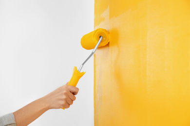 Photo of Woman painting white wall with yellow dye, closeup. Interior renovation