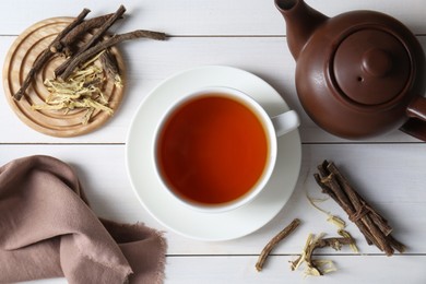 Photo of Aromatic licorice tea in cup and dried sticks of licorice root on white wooden table, flat lay
