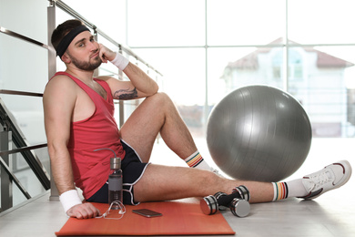 Photo of Lazy young man with sport equipment on yoga mat indoors