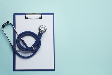Photo of Clipboard with stethoscope on turquoise background, top view. Space for text