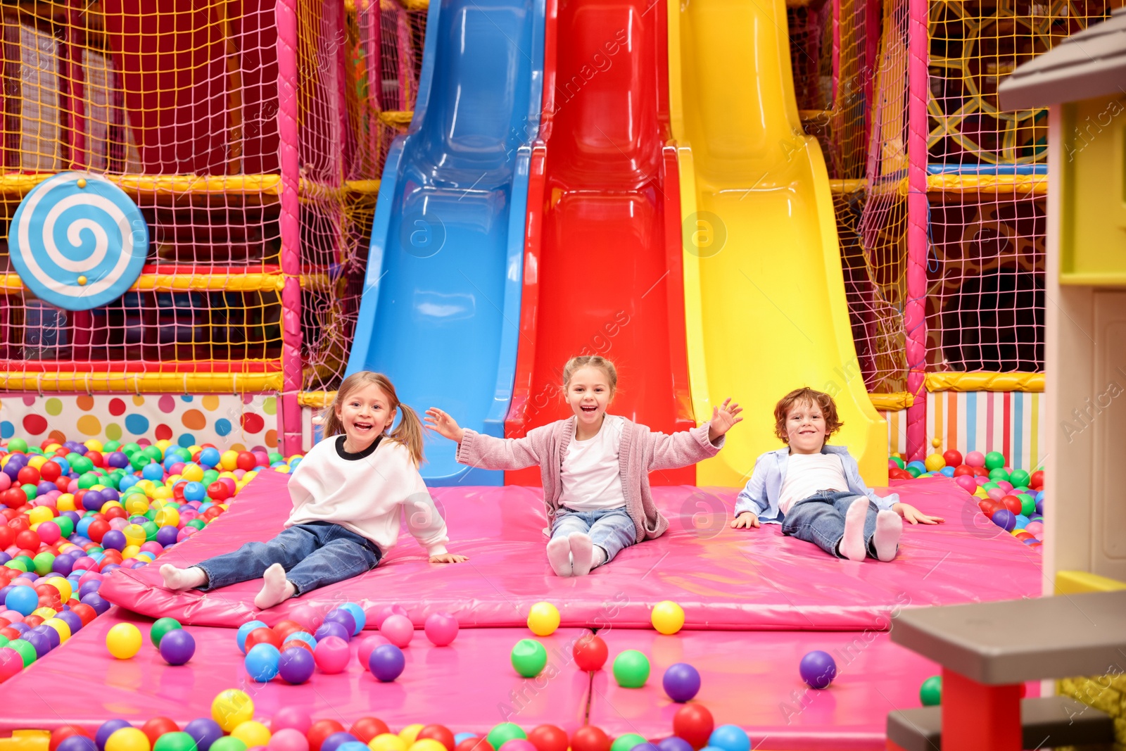 Photo of Happy kids playing in play room with slides, mats and ball pit