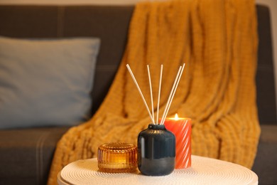 Aromatic reed air freshener and scented candles on wooden table indoors