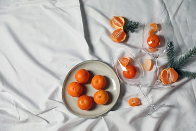 Delicious fresh ripe tangerines and glasses on white bedsheet, flat lay. Space for text