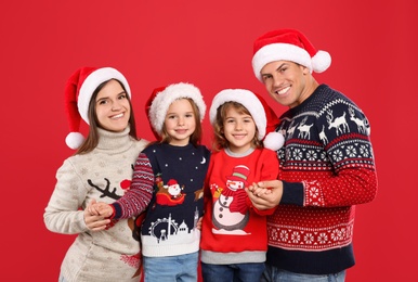 Family in Christmas sweaters and Santa hats on red background