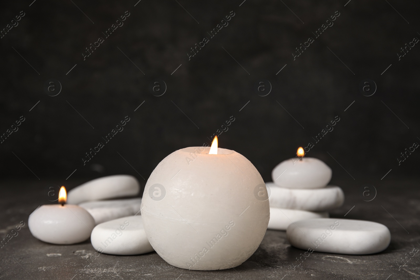 Photo of Burning candles and white spa stones on grey table