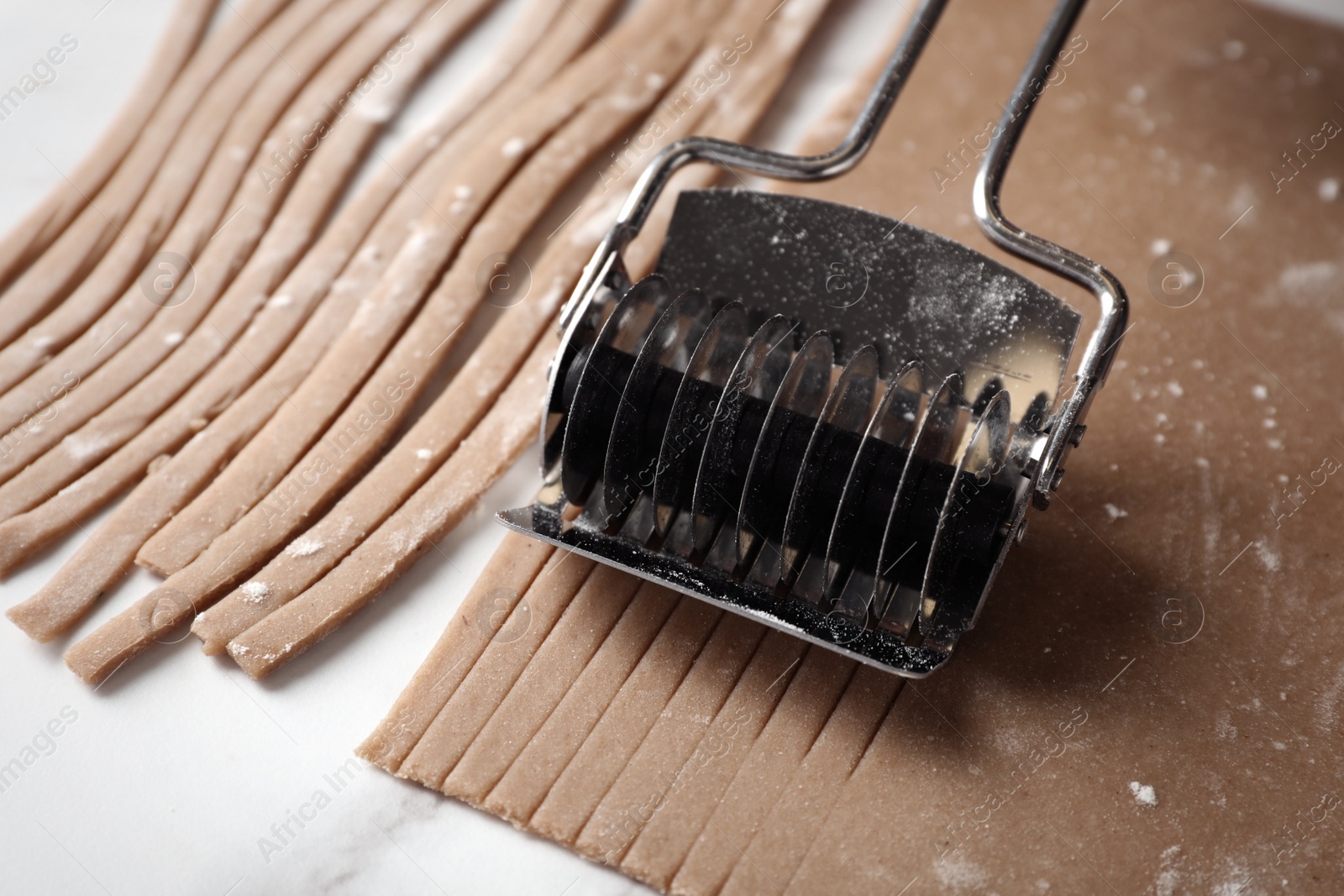 Photo of Making soba (buckwheat noodles) with cutter at white marble table, closeup