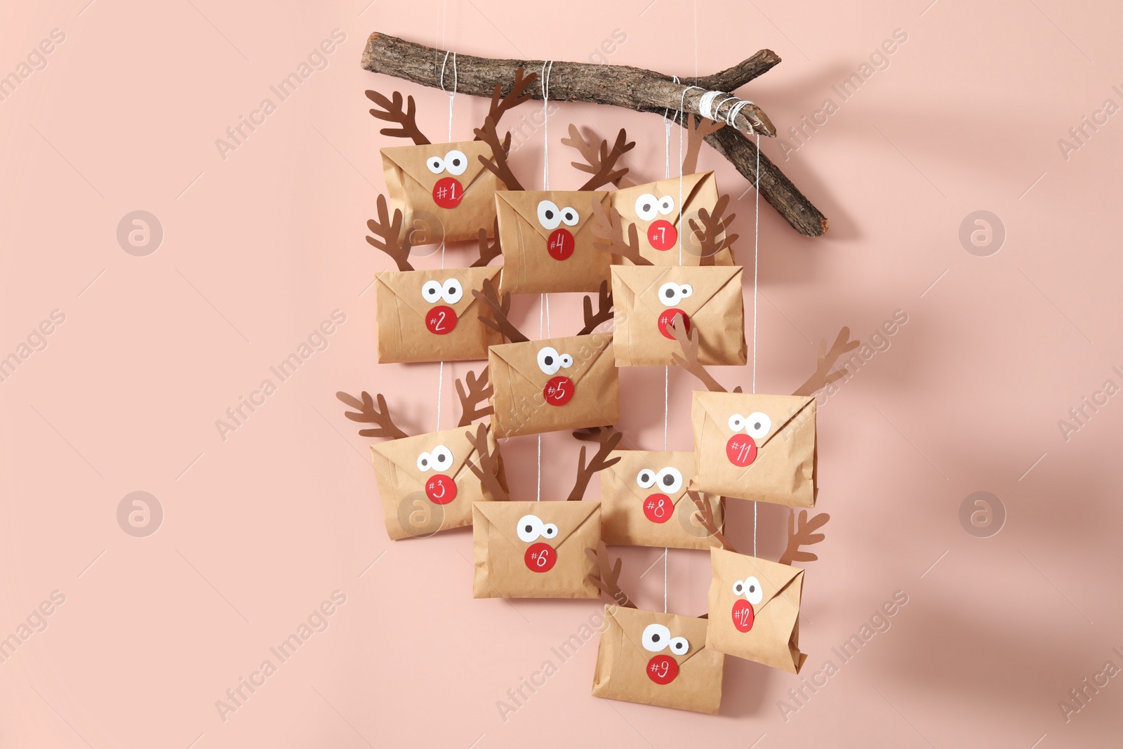 Photo of Gifts in envelopes with deer faces hanging on pink wall. Christmas advent calendar