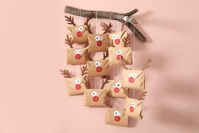 Photo of Gifts in envelopes with deer faces hanging on pink wall. Christmas advent calendar