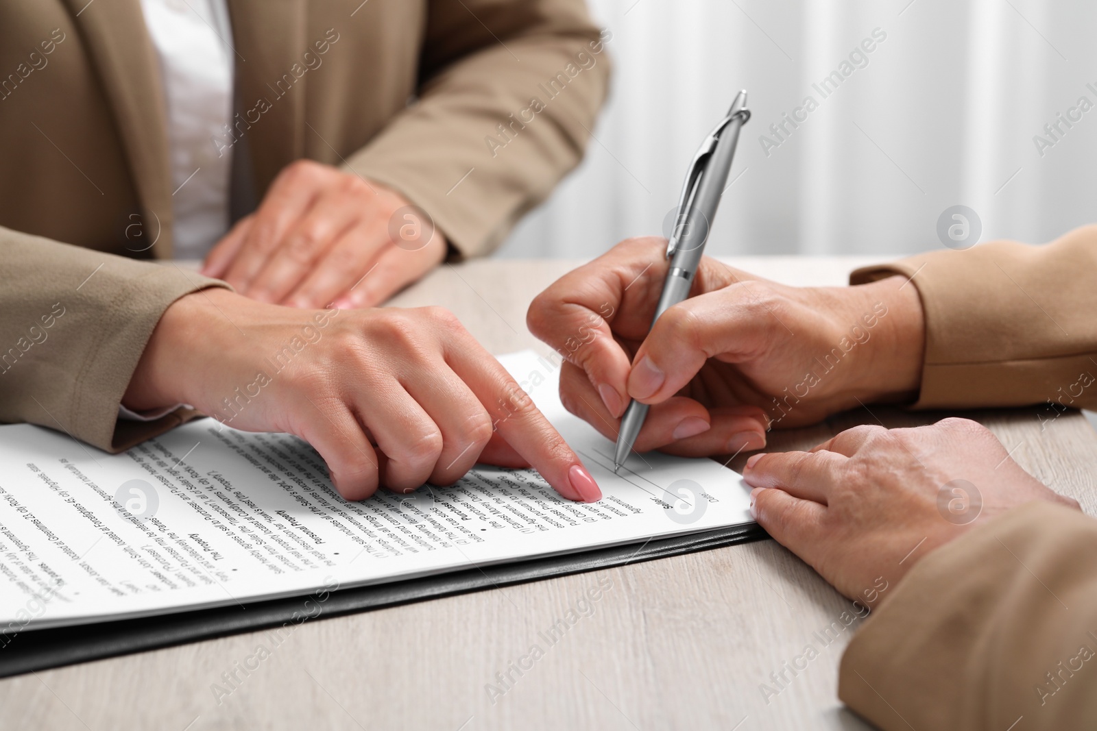 Photo of Manager showing client where she must to mark signature at light wooden table indoors, closeup