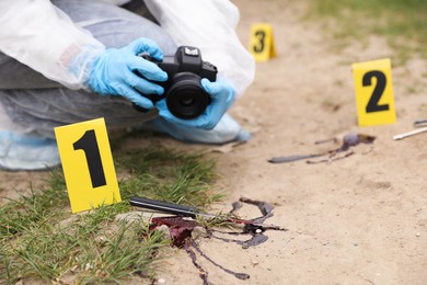 Photo of Criminologist in protective suit taking photo of evidence at crime scene outdoors, closeup. Space for text