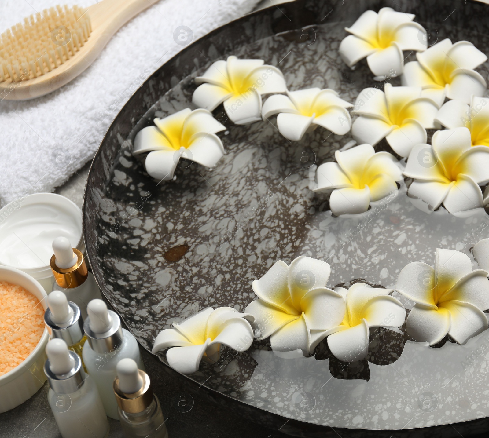 Photo of Bowl of water with flowers and different spa supplies on table