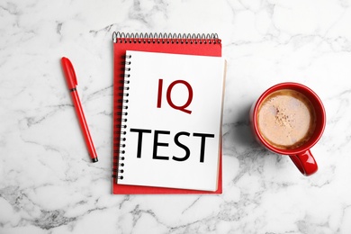 Notebook with text IQ Test, pen and cup of coffee on white marble table, flat lay