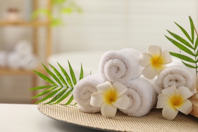 Photo of Spa composition. Towels, plumeria flowers and palm leaves on white table in bathroom