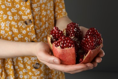 Woman holding fresh pomegranate on dark background, closeup