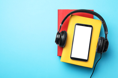 Books with modern headphones and smartphone on light blue background, top view. Space for text