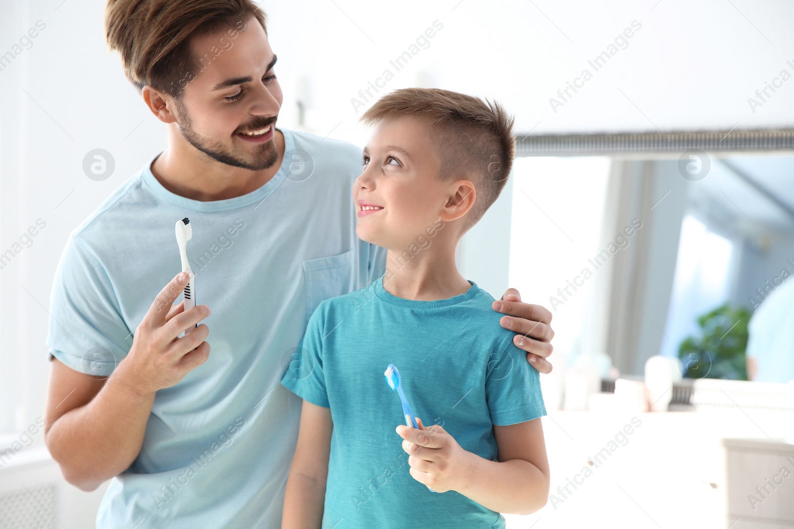 Photo of Young man and his son with toothbrushes in bathroom, space for text. Personal hygiene