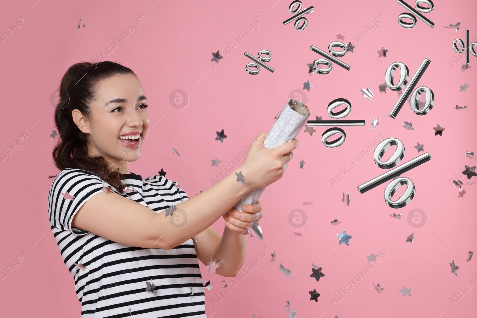 Image of Discount offer. Happy young woman blowing up party popper on pink background. Confetti and percent signs in air