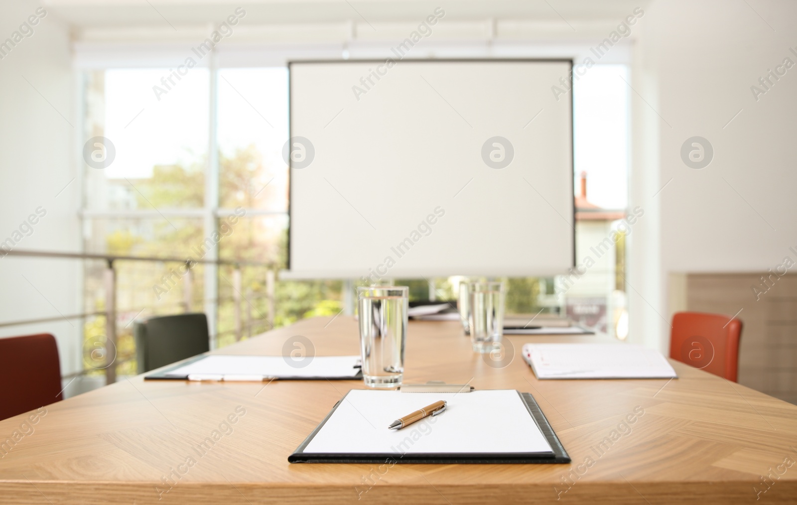 Photo of Clipboards and glasses of water on wooden table in modern office with projection screen