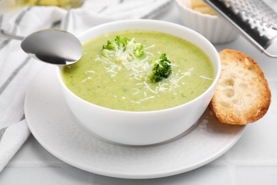 Photo of Delicious broccoli cream soup with cheese served on white tiled table, closeup