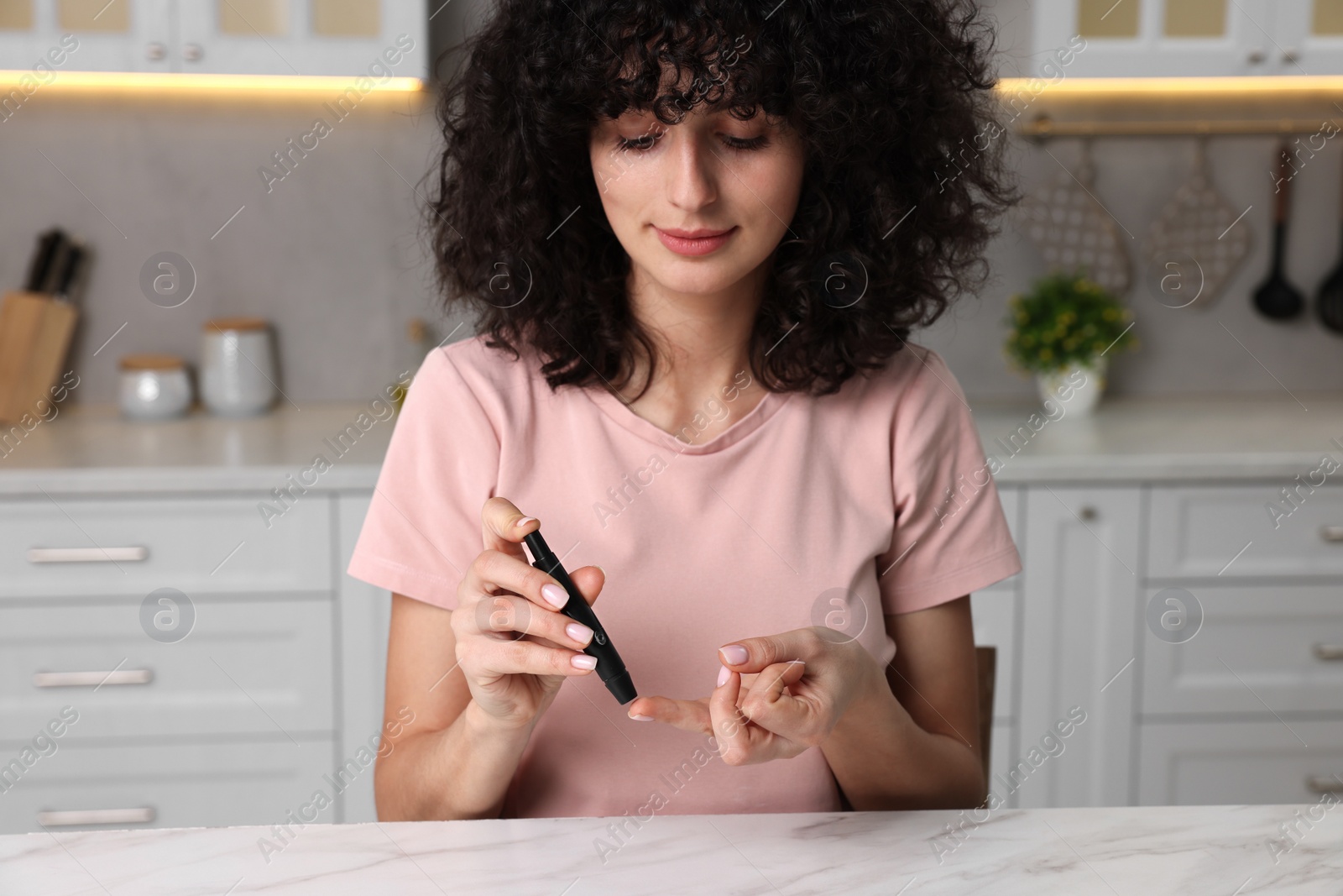 Photo of Diabetes. Woman using lancet pen at white marble table in kitchen