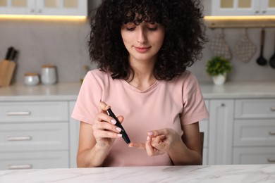 Diabetes. Woman using lancet pen at white marble table in kitchen