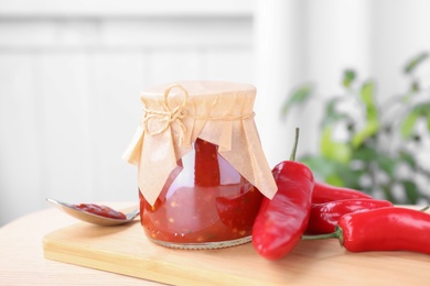 Photo of Glass jar of hot chili sauce with peppers on table