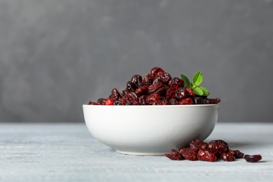 Photo of Tasty dried cranberries and leaves on wooden table against grey background