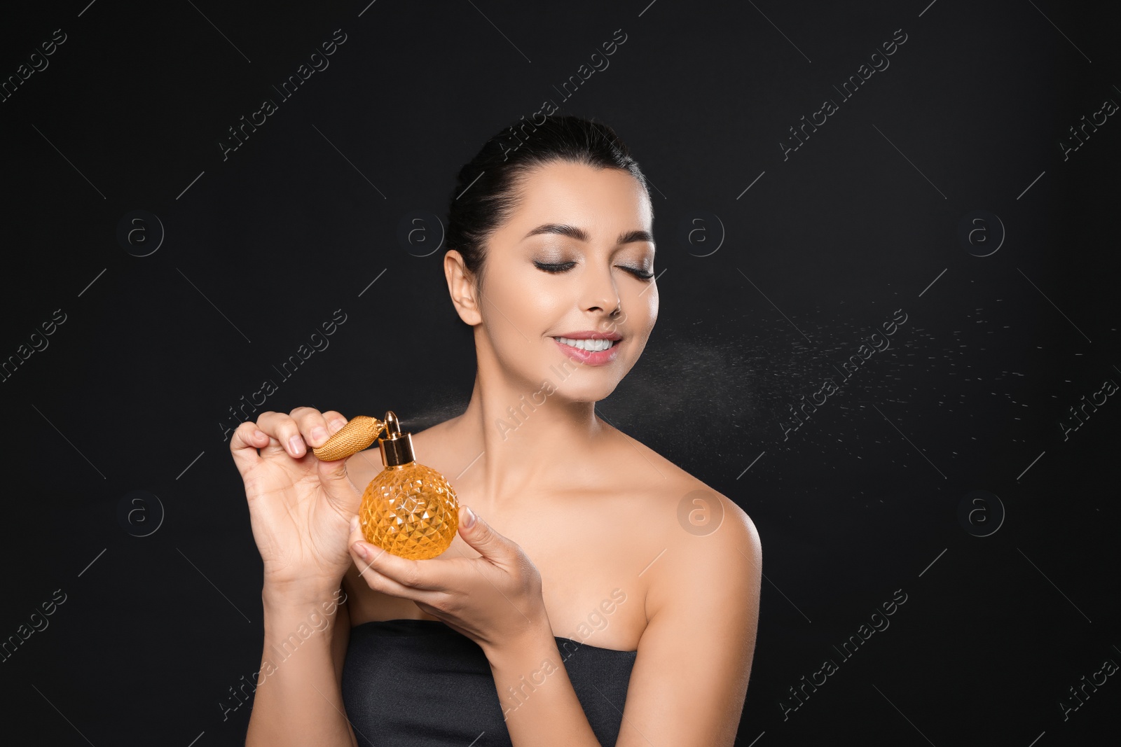 Photo of Young woman spraying perfume on black background