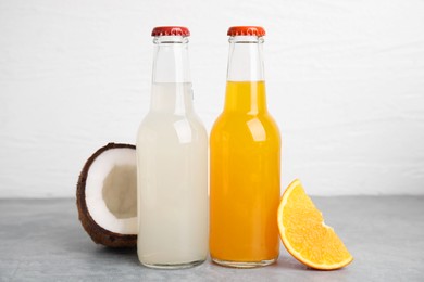 Photo of Delicious kombucha in glass bottles, coconut and orange on grey table against white background