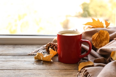 Cup of hot drink, scarf and autumn leaves on windowsill, space for text. Cozy atmosphere