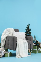 Photo of Beautiful Christmas themed photo zone with stylish armchair, trees and gift boxes on light blue background