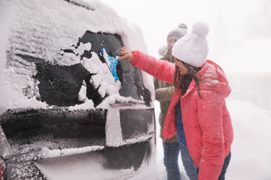 Photo of Man cleaning snow from car outdoors on winter day