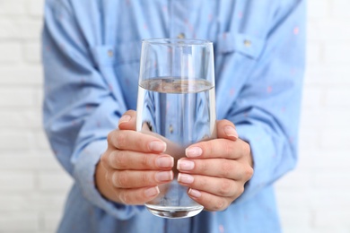 Photo of Woman holding glass of water near brick wall, closeup. Refreshing drink