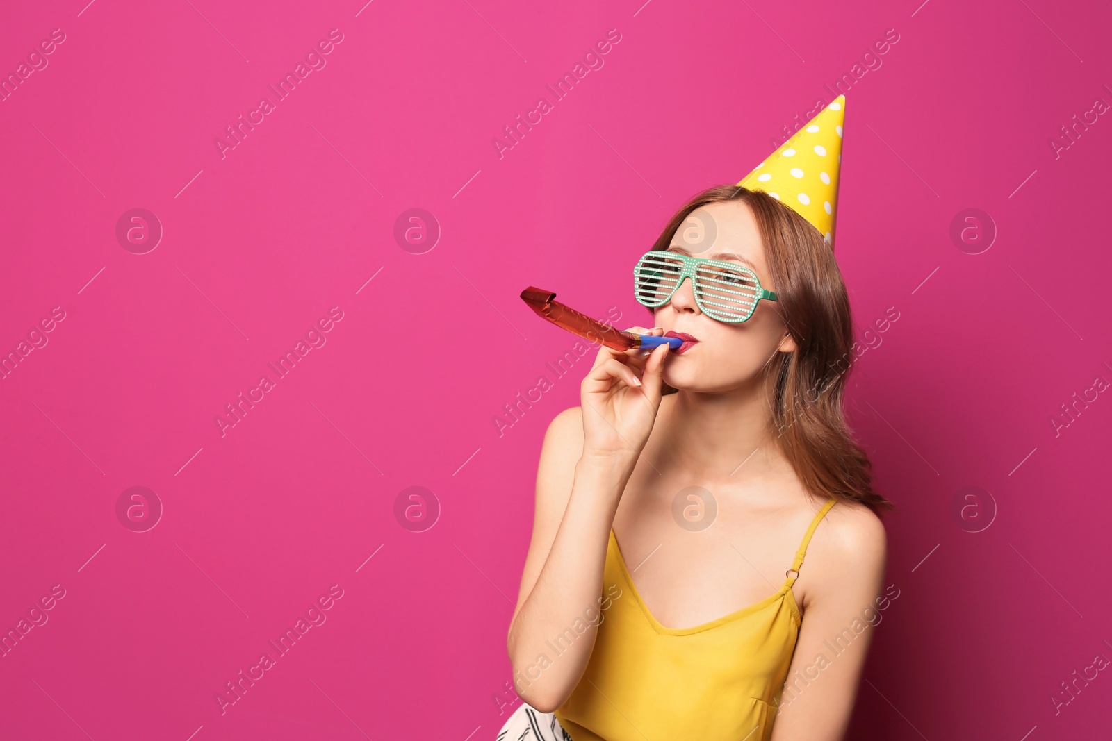 Photo of Young woman with party blower on color background. Birthday celebration