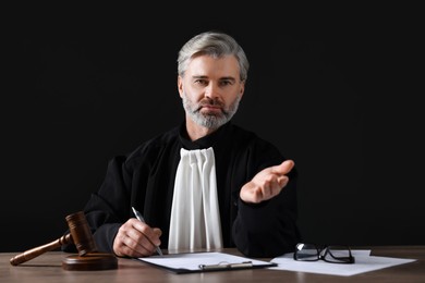 Photo of Judge with gavel and papers sitting at wooden table against black background