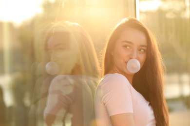 Beautiful young woman blowing bubble gum outdoors on sunny day. Space for text