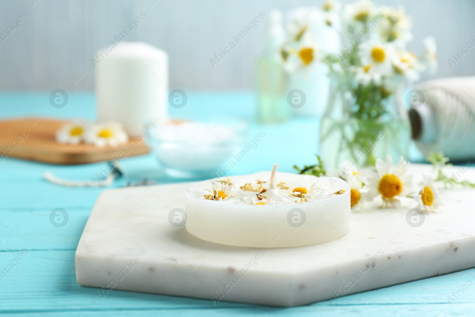 Photo of Board with floral candle and chamomile on color wooden table