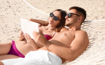 Photo of Young couple with tablet relaxing in hammock on beach