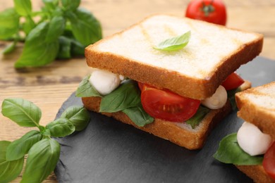 Photo of Delicious Caprese sandwiches with mozzarella, tomatoes, basil and pesto sauce on wooden table, closeup