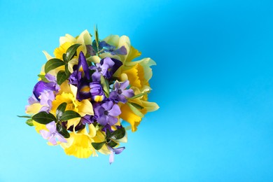 Photo of Bouquet of beautiful yellow daffodils, iris and periwinkle flowers on light blue background, top view. Space for text