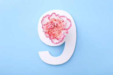 Paper number 9 and beautiful flower on light blue background, top view