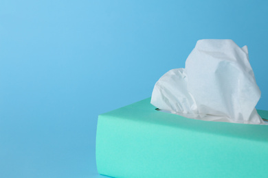 Photo of Box of paper tissues on light blue background, closeup. Space for text