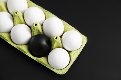 Photo of Black egg among others in box on color background, top view