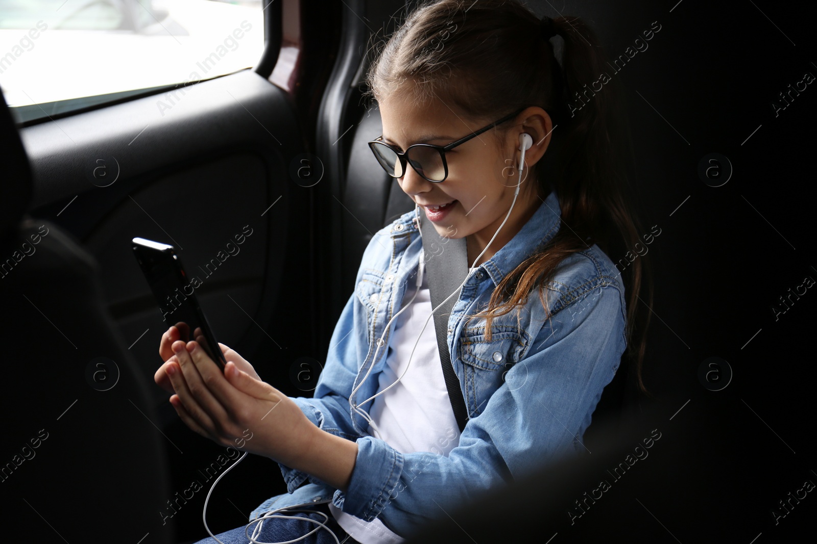 Photo of Cute little girl listening to audiobook in car