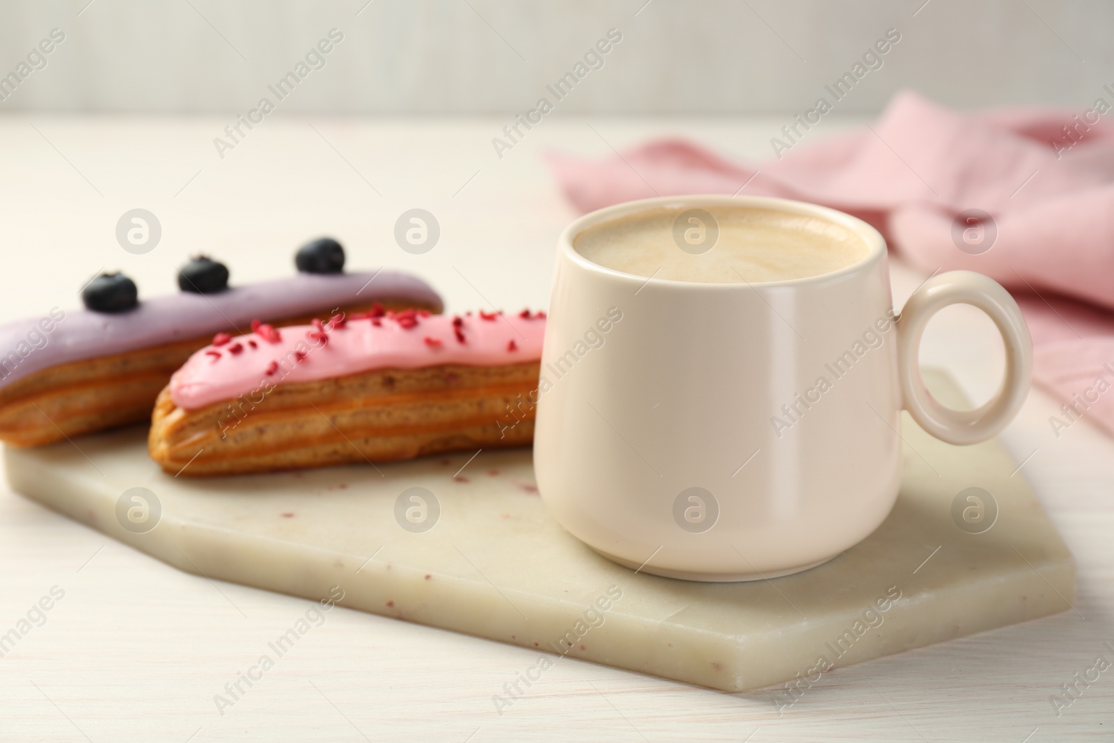 Photo of Cup of coffee and delicious eclairs covered with glaze on white wooden table